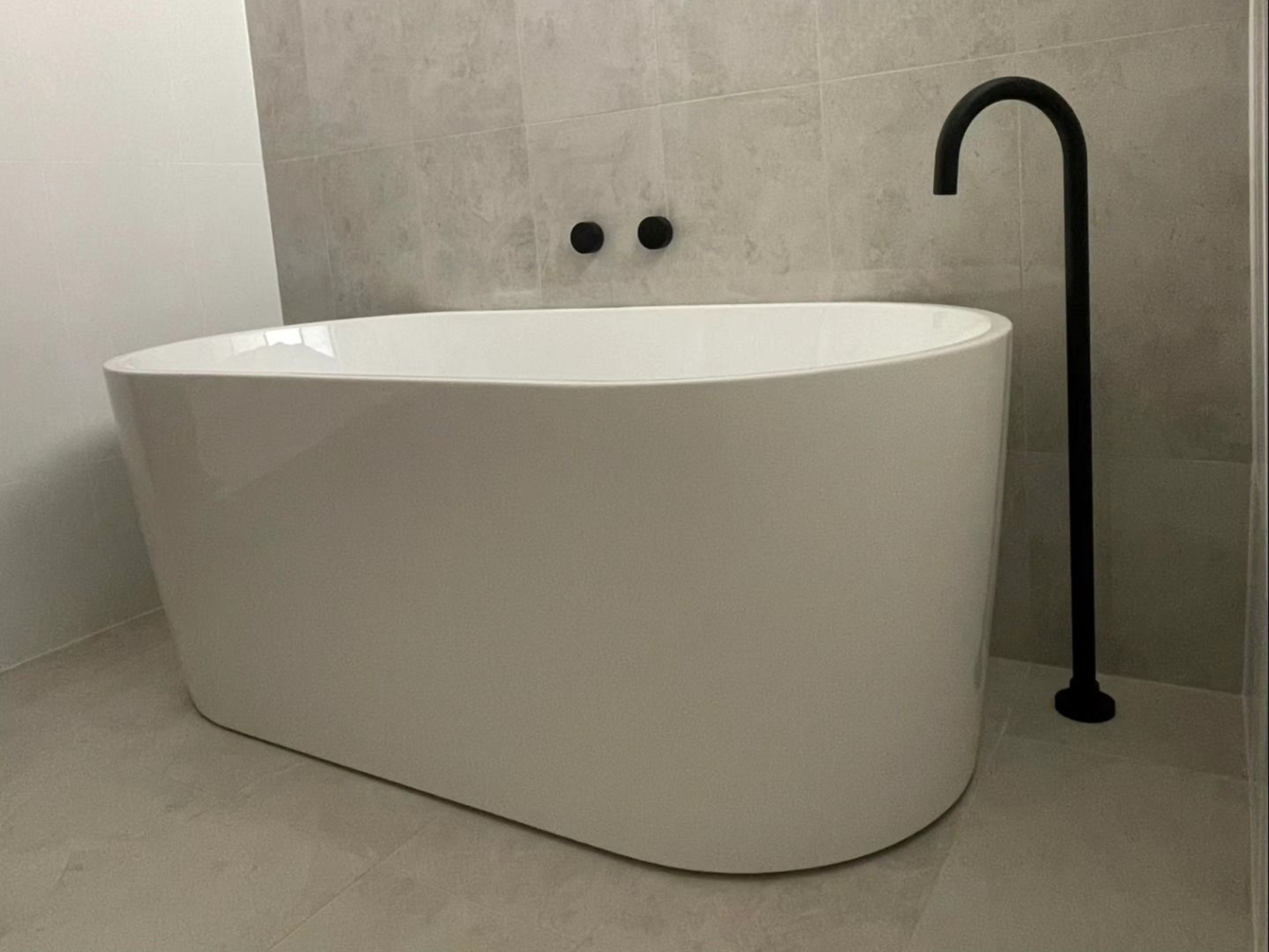 Modern freestanding white bathtub with black floor-mounted faucet in a minimalist bathroom