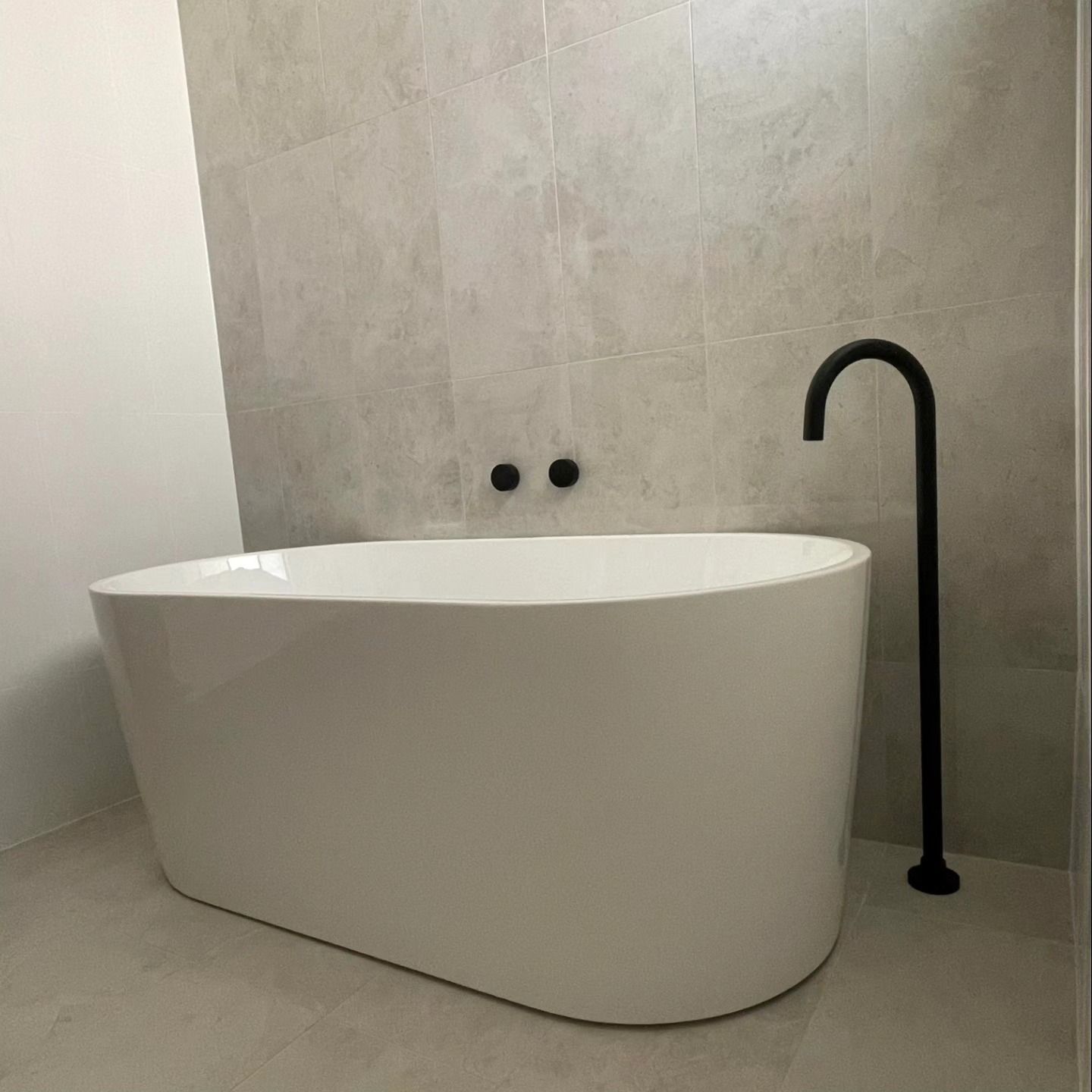 Modern bathroom with a white freestanding bathtub, black floor faucet, and light stone walls