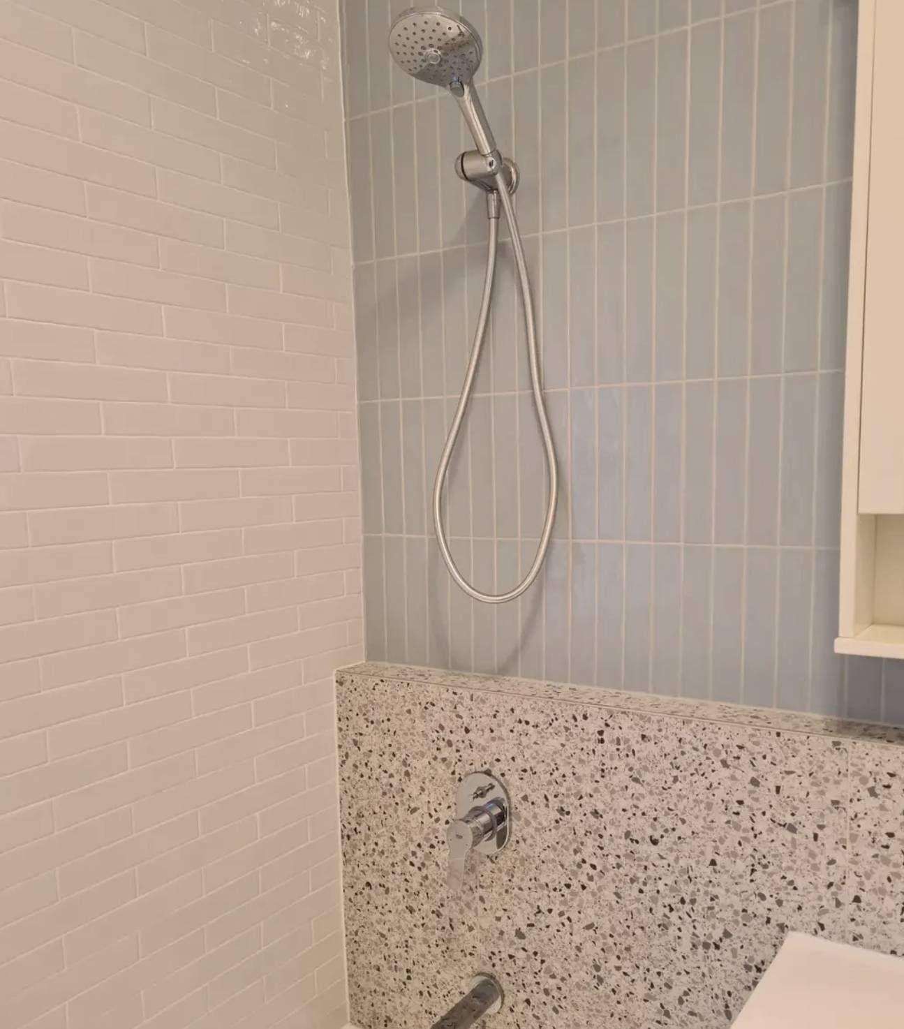 Shower with handheld showerhead and speckled tub surround in a small bathroom.