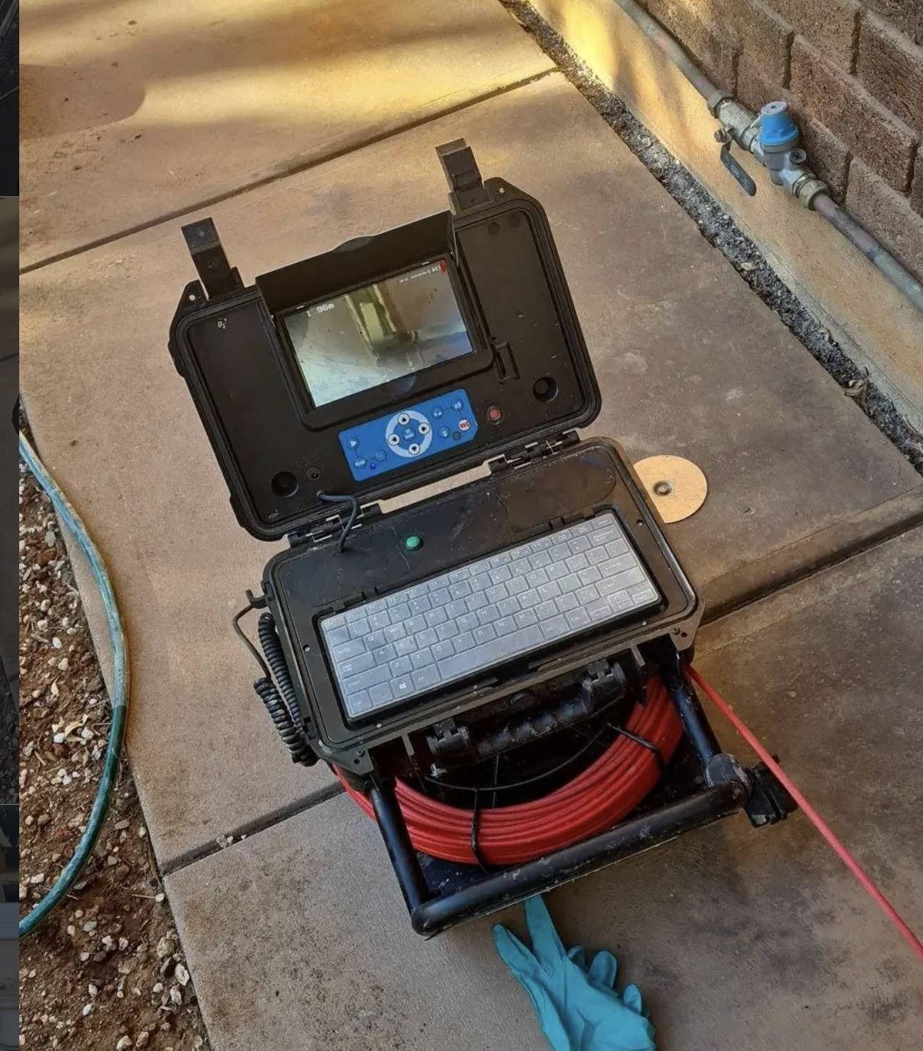Open inspection camera with display and coiled red cable on pavement