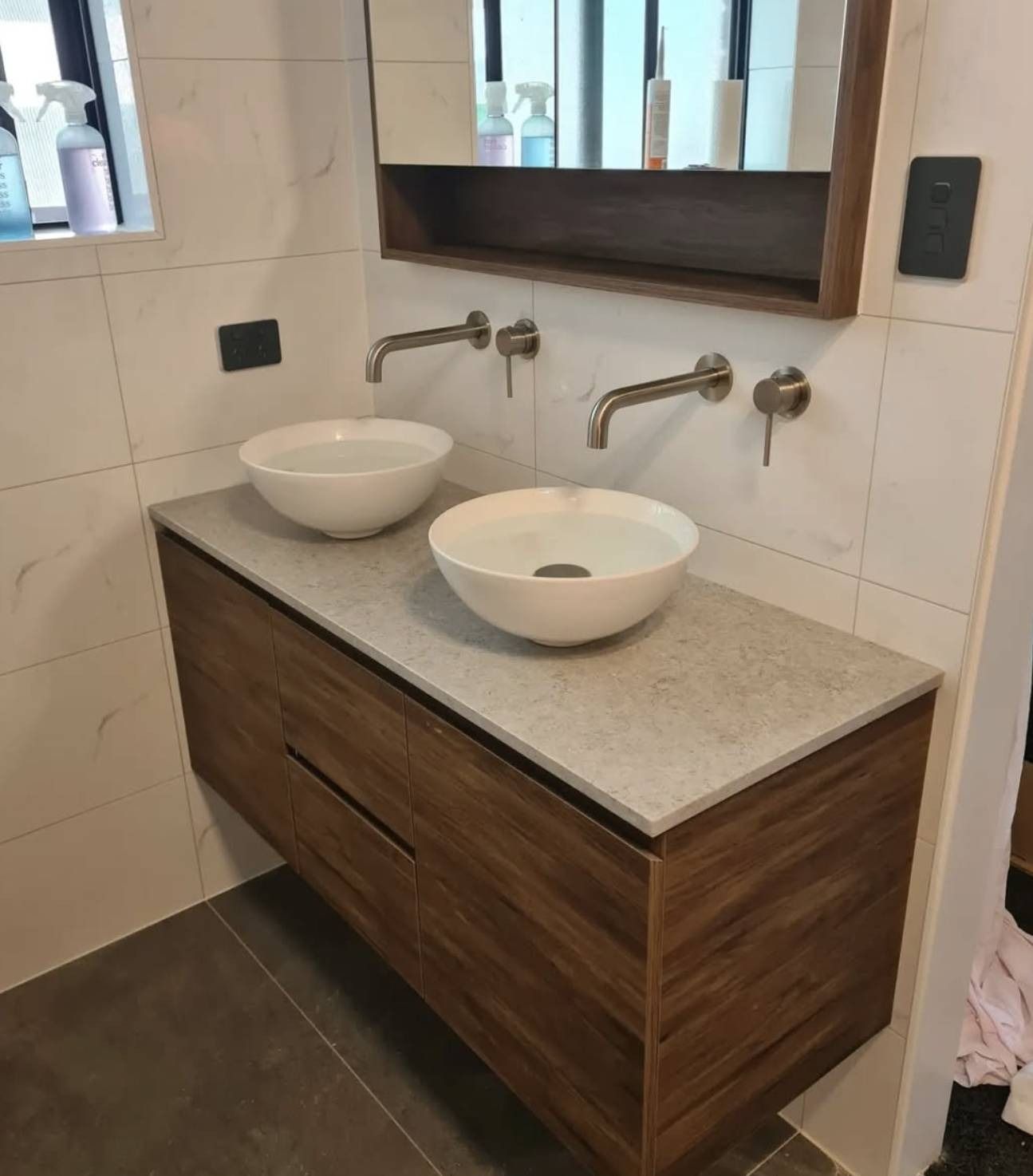 Double sink vanity with wood cabinet and mirror in a tiled bathroom