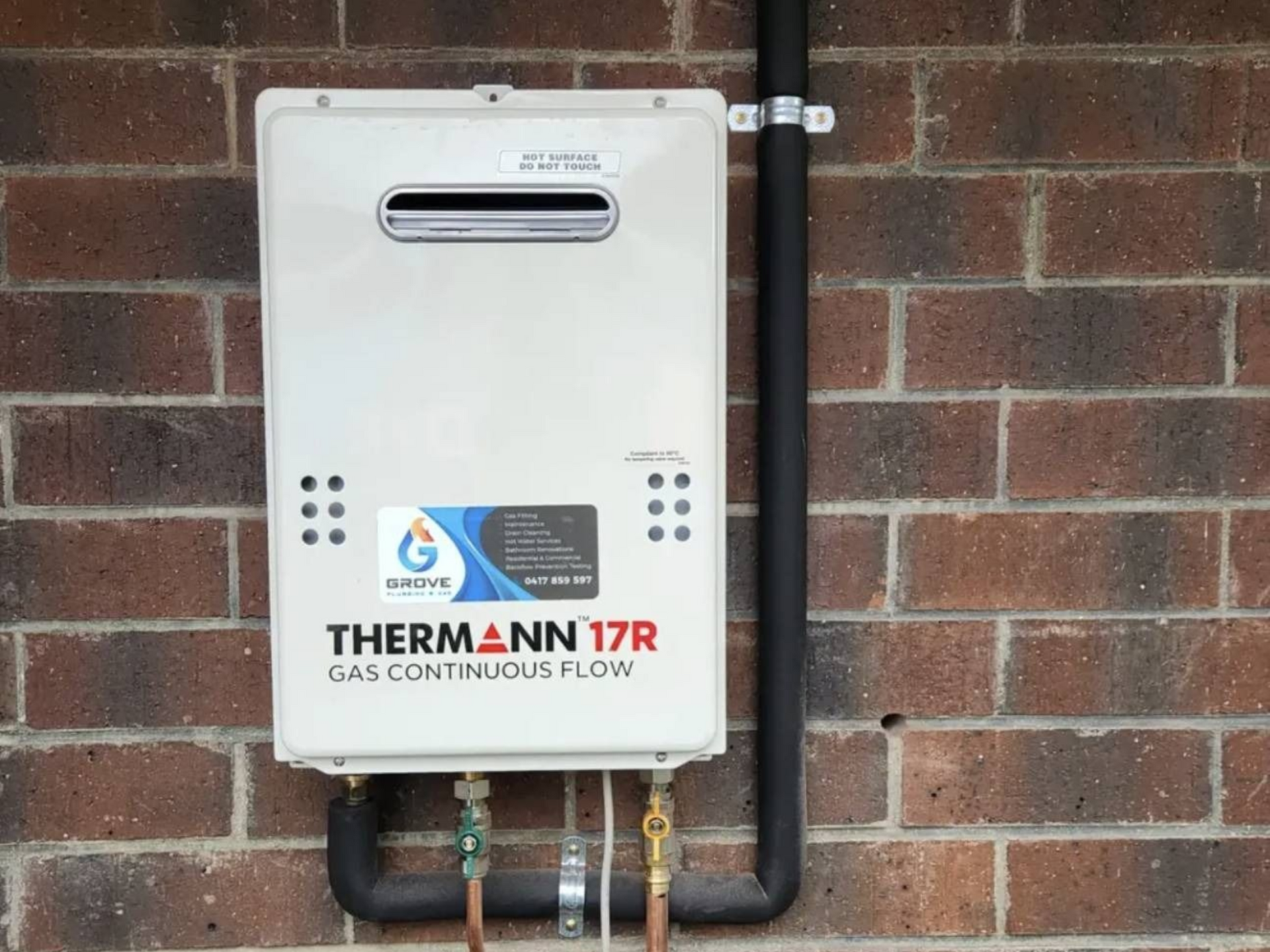 Man standing by a brick wall holding a box beside a window and hose reel