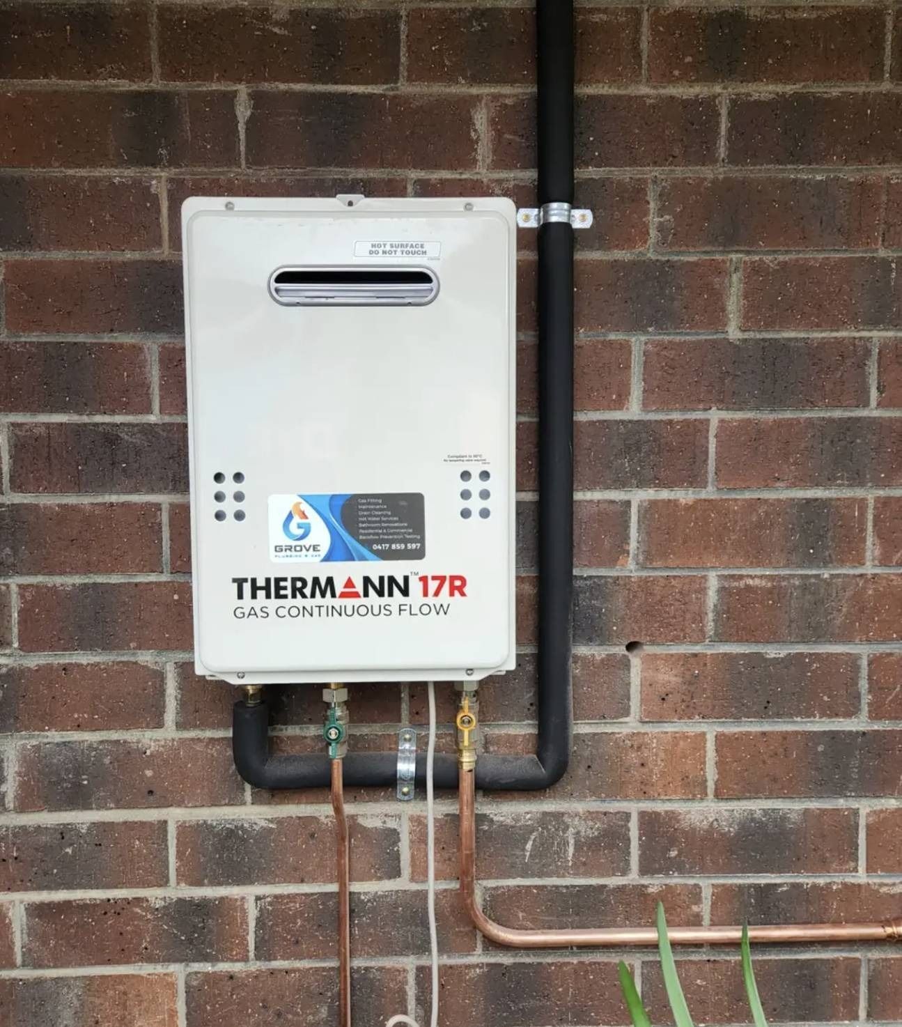 White gas meter box mounted on a brick wall with black and copper pipes underneath