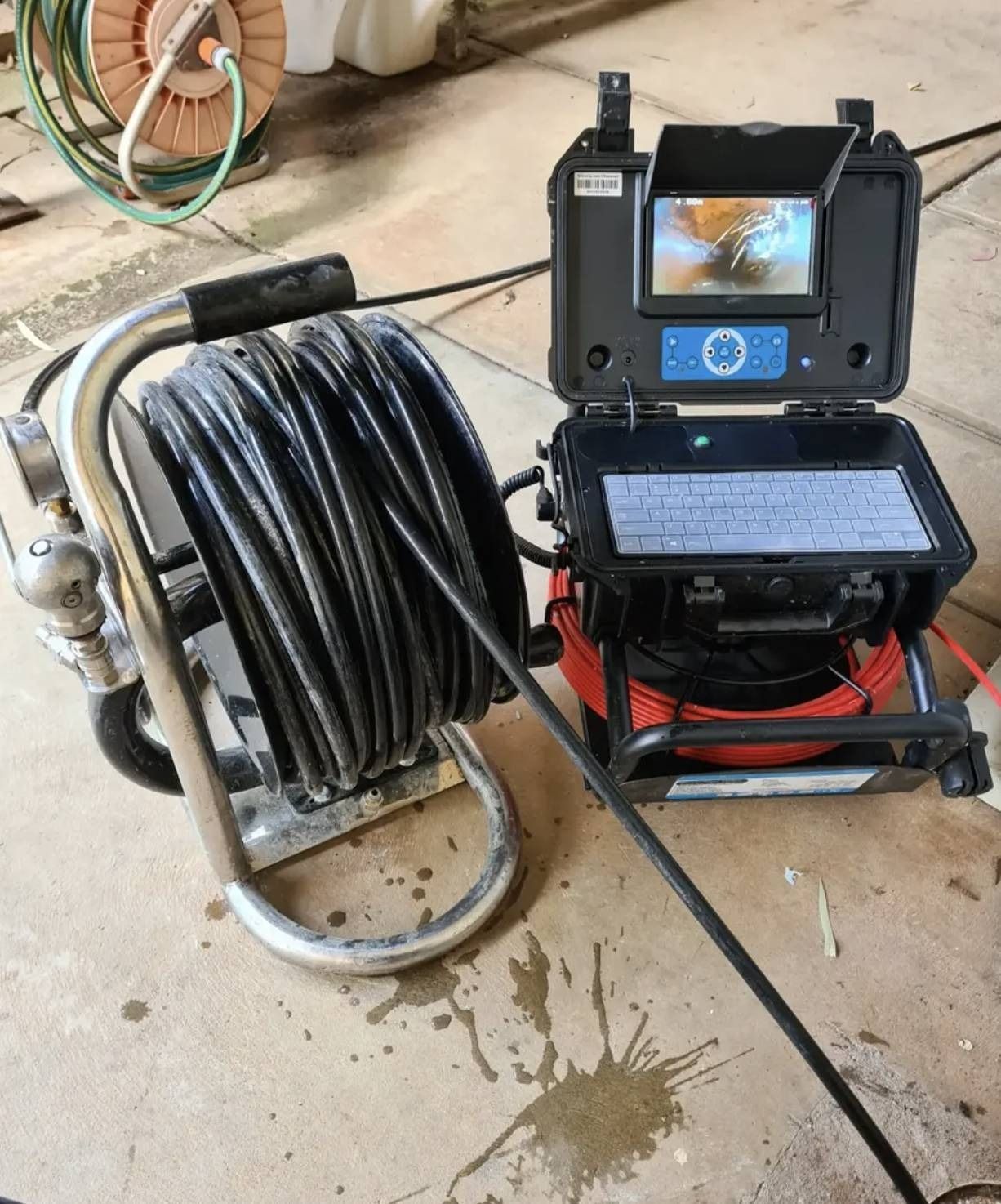 Industrial drain inspection camera with coiled black cable on a wheeled frame in a workshop area