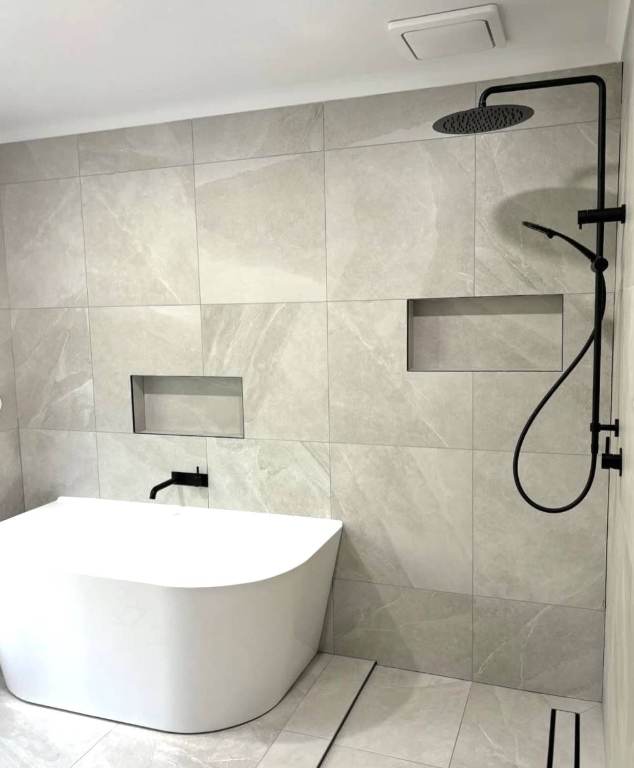 Modern bathroom with freestanding tub and black rainfall shower against large gray tiled wall