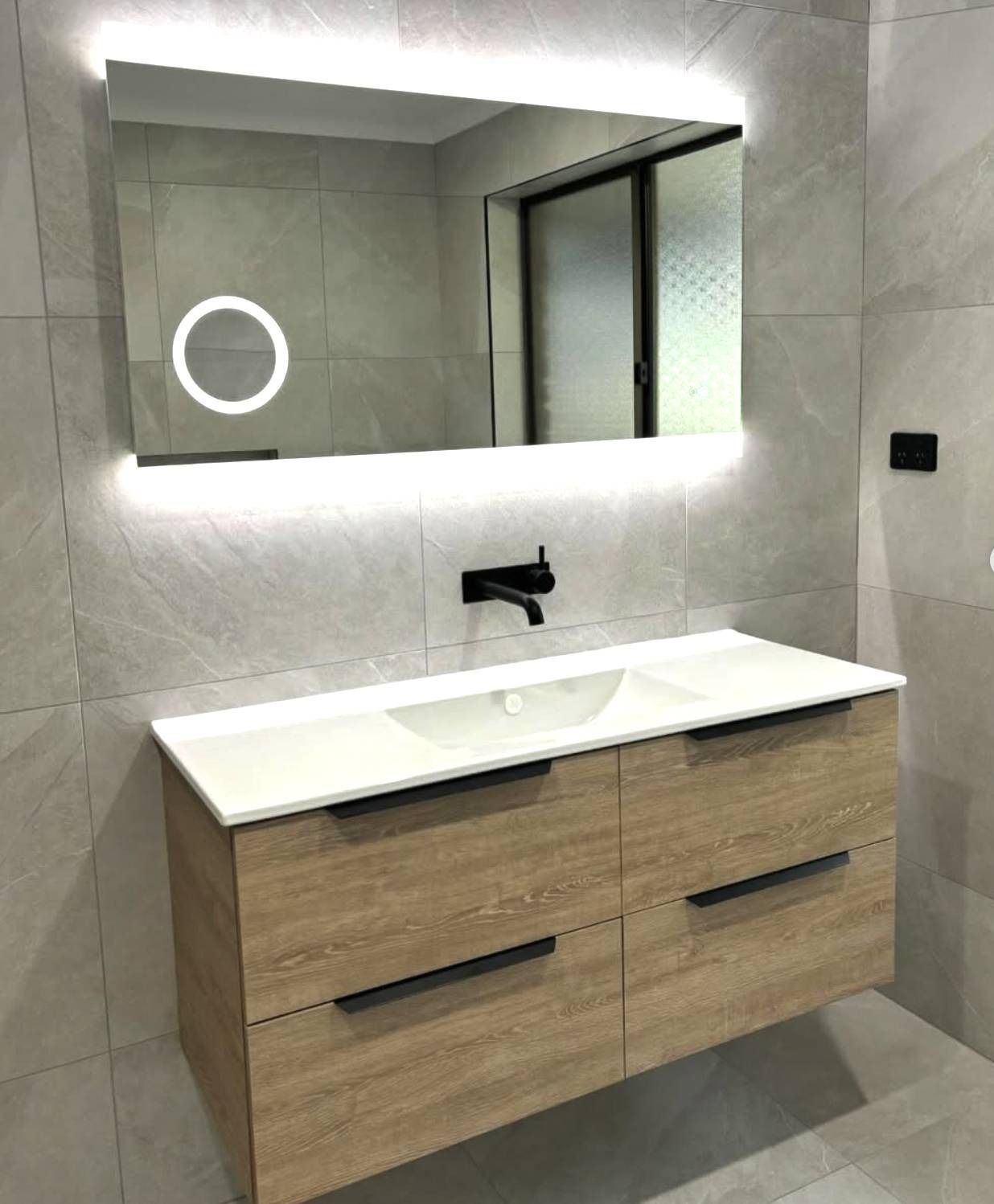 Modern bathroom vanity with white sink, wood cabinet, backlit mirror, and round LED light.