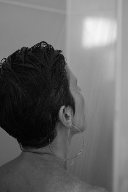 Person with wet hair rinsing under a shower in a tiled bathroom
