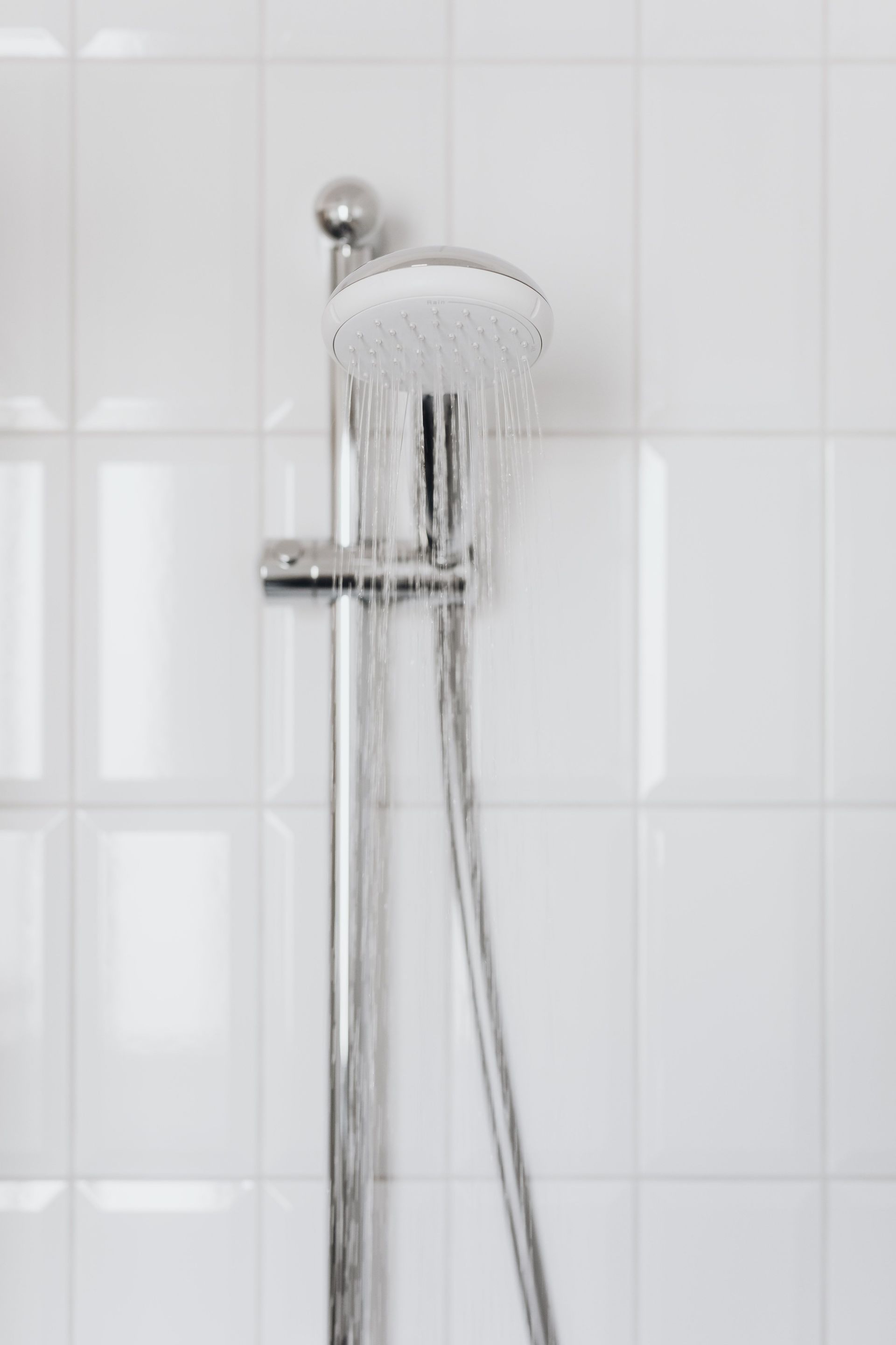 Chrome showerhead in a white tiled bathroom, spraying water.