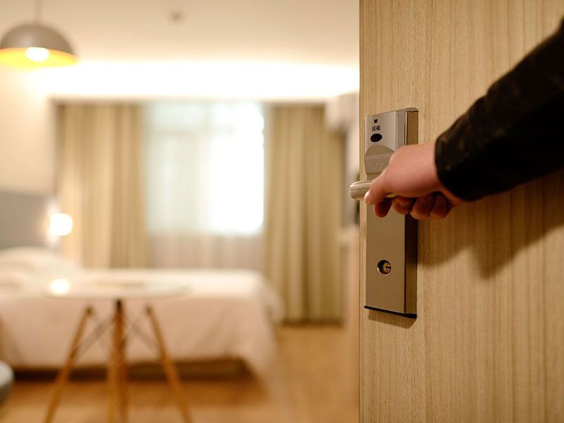 Abrindo a porta de um quarto de hotel, revelando um quarto com cama, mesa e janela.