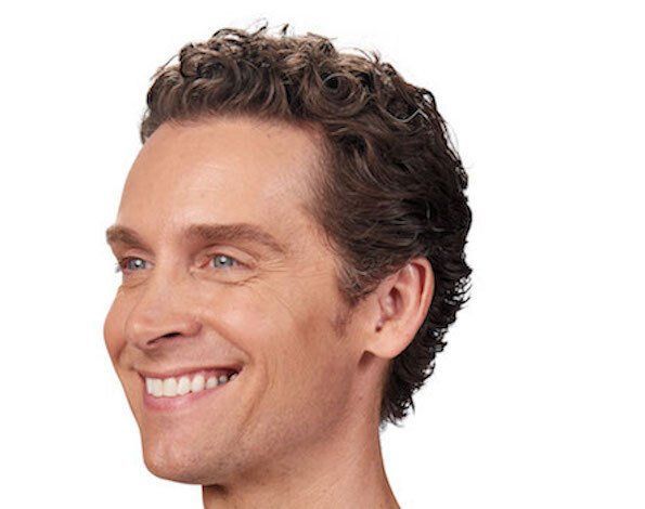 Man with curly brown hair smiles, looking towards the left.
