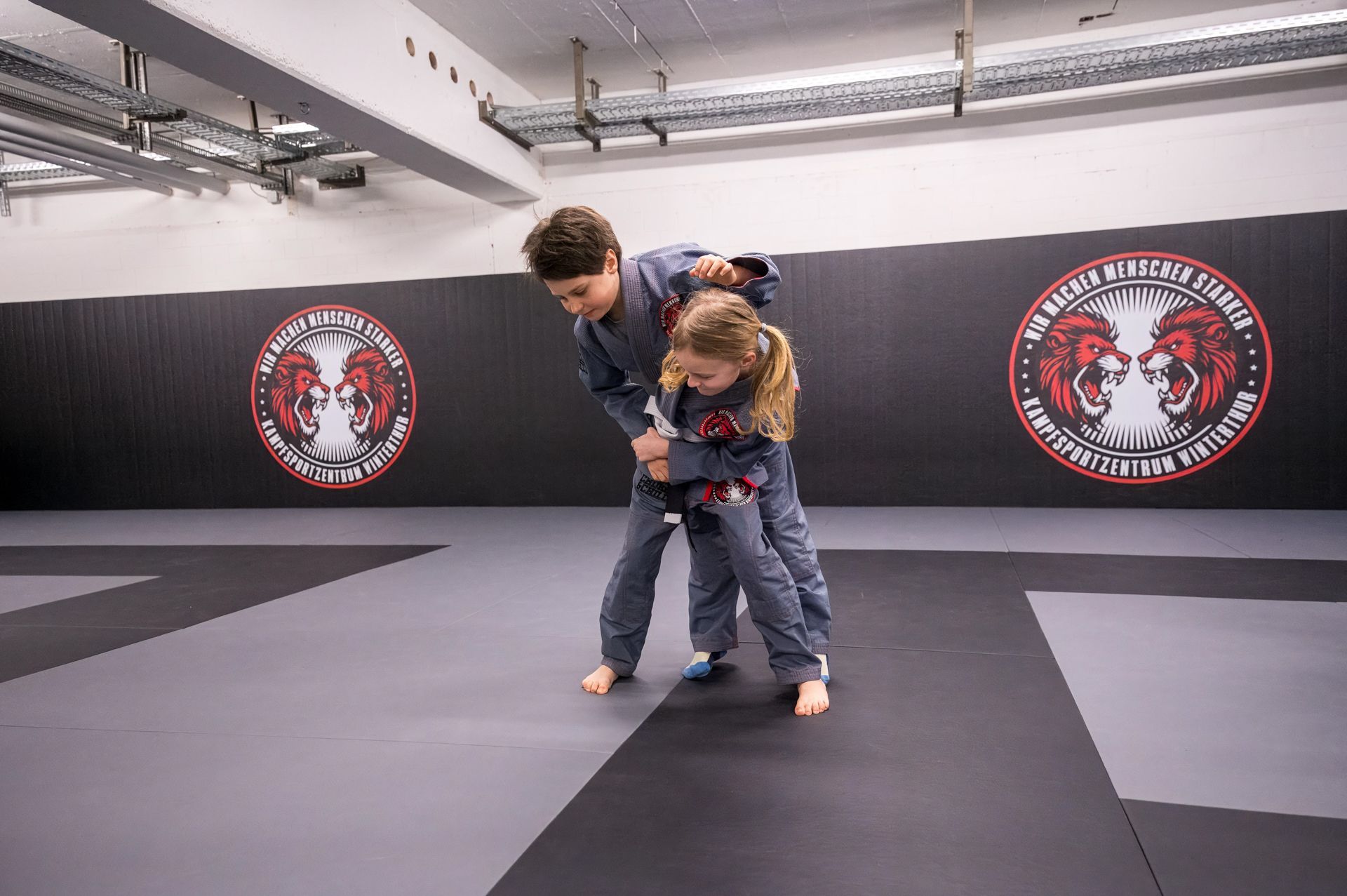 Ein Junge und ein Mädchen trainieren Jiu Jitsu in einem Kampfsportzentrum.