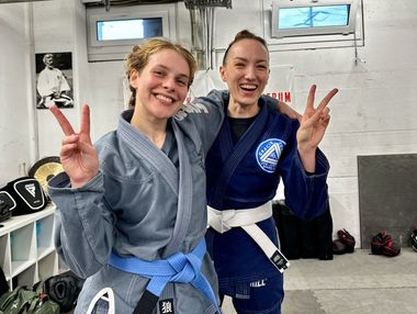 Zwei Frauen in Karateuniformen machen ein Peace-Zeichen.