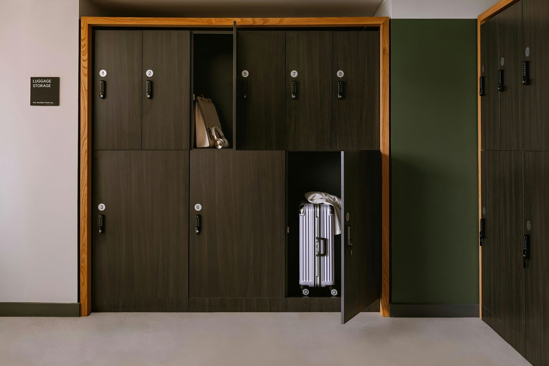 Dark wood lockers in a modern interior, with one open to reveal a silver rolling suitcase inside.