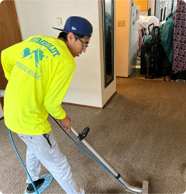 Person in yellow shirt vacuums a carpet in a room.
