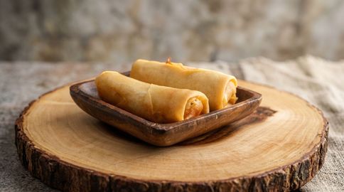 Two golden rolled pastries on a wooden plate atop a tree stump table