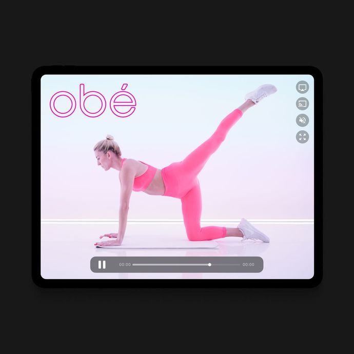A woman in pink activewear does a leg lift exercise on a tablet screen. The screen displays the 
