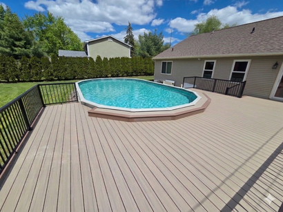 A round above-ground pool surrounded by a custom octagonal wood deck on a gray wooden patio in a backyard.