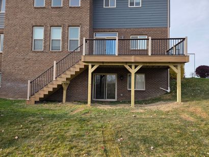 A rustic log cabin with a light-colored wooden deck, framed by green landscaping and mulch, set against a sunny sky.
