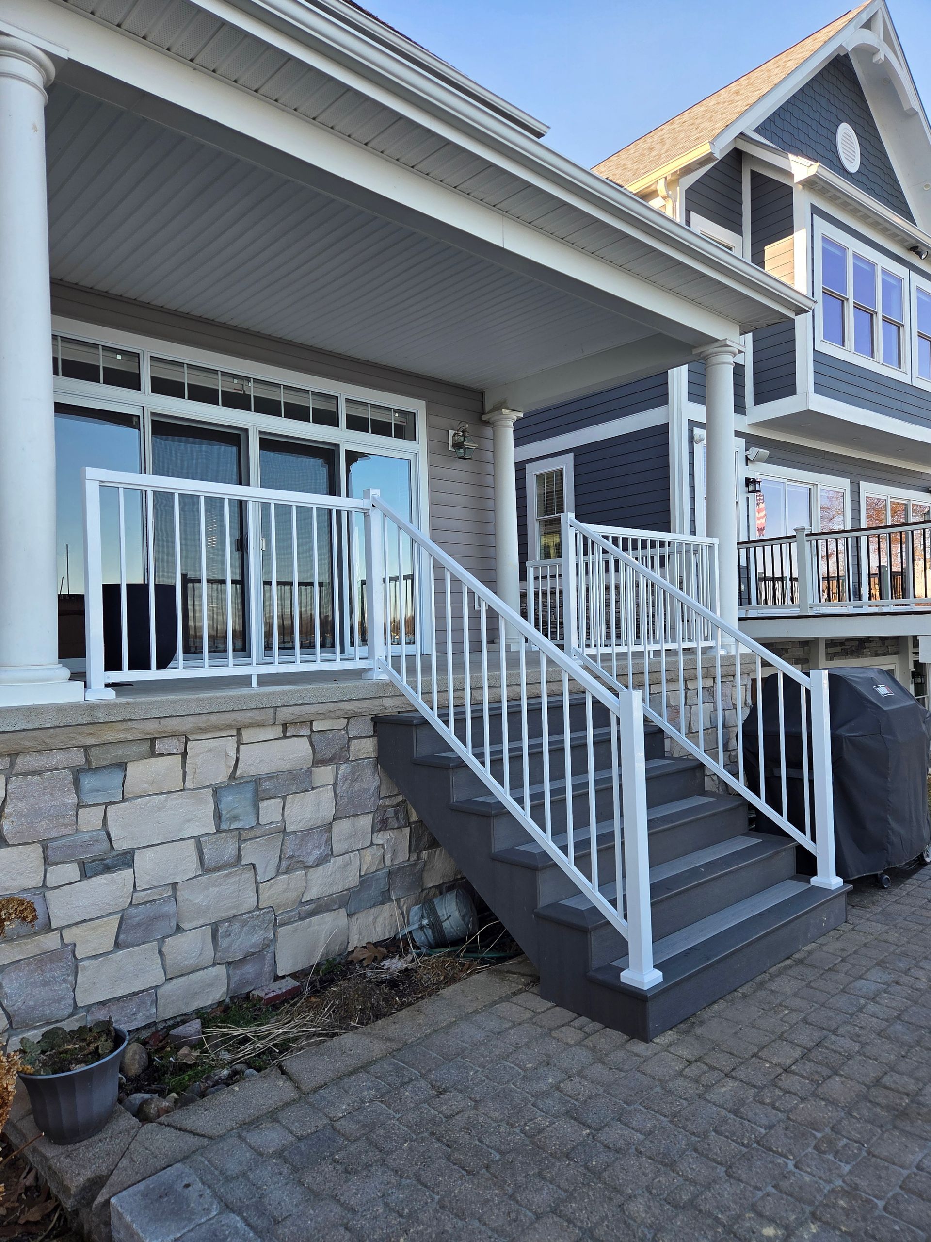 A wide, elevated composite deck with white railings overlooks a backyard with trees under a clear blue sky.