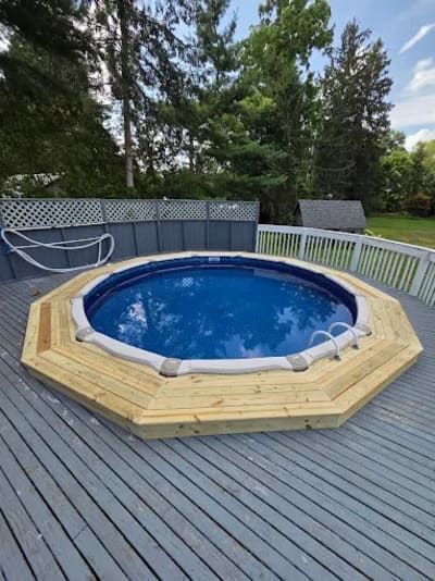 A round above-ground pool set into a wooden octagon deck, surrounded by a gray privacy fence and a larger deck area.