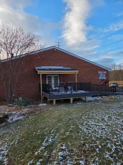 A brick building with a new wooden deck, a covered porch, and a metal railing set against a blue, partly cloudy sky.