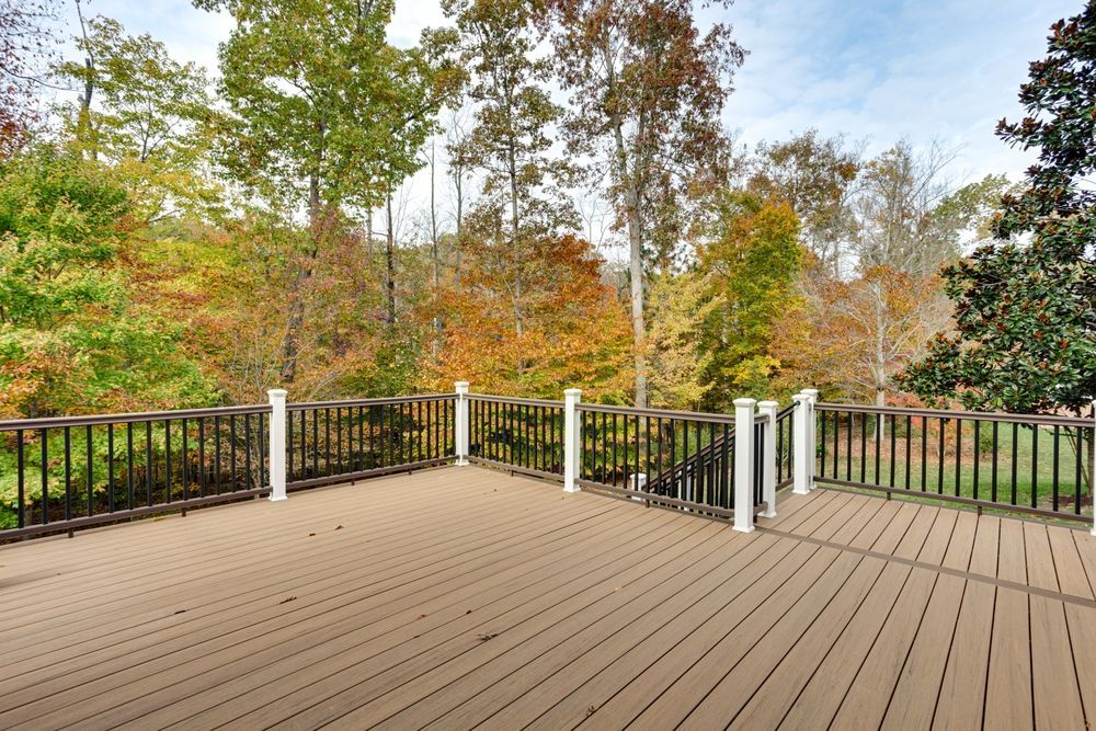 An empty, elevated wooden deck with a black railing, overlooking a background of trees in autumn foliage.