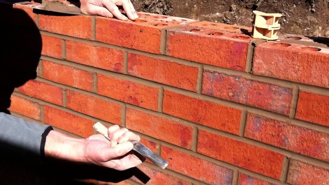 Person laying red bricks with mortar on a brick wall under construction
