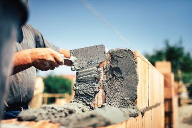 Worker applying mortar to a brick wall under construction