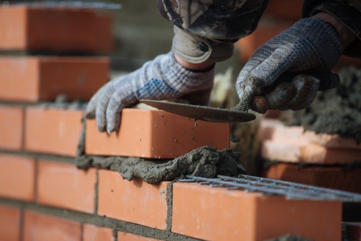 Gloved hands placing a brick on a mortar-covered brick wall during construction