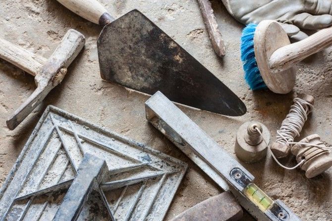 Masonry tools and a tile trowel on dusty ground next to a patterned tile