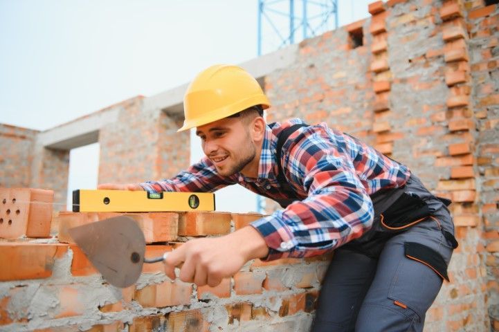 Construction worker in yellow hard hat laying bricks with a trowel and level