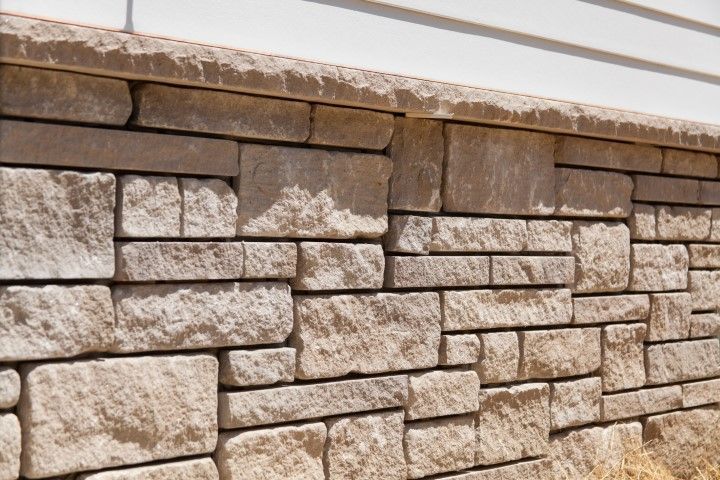 Stone retaining wall with tan and gray blocks beneath a white ledge.