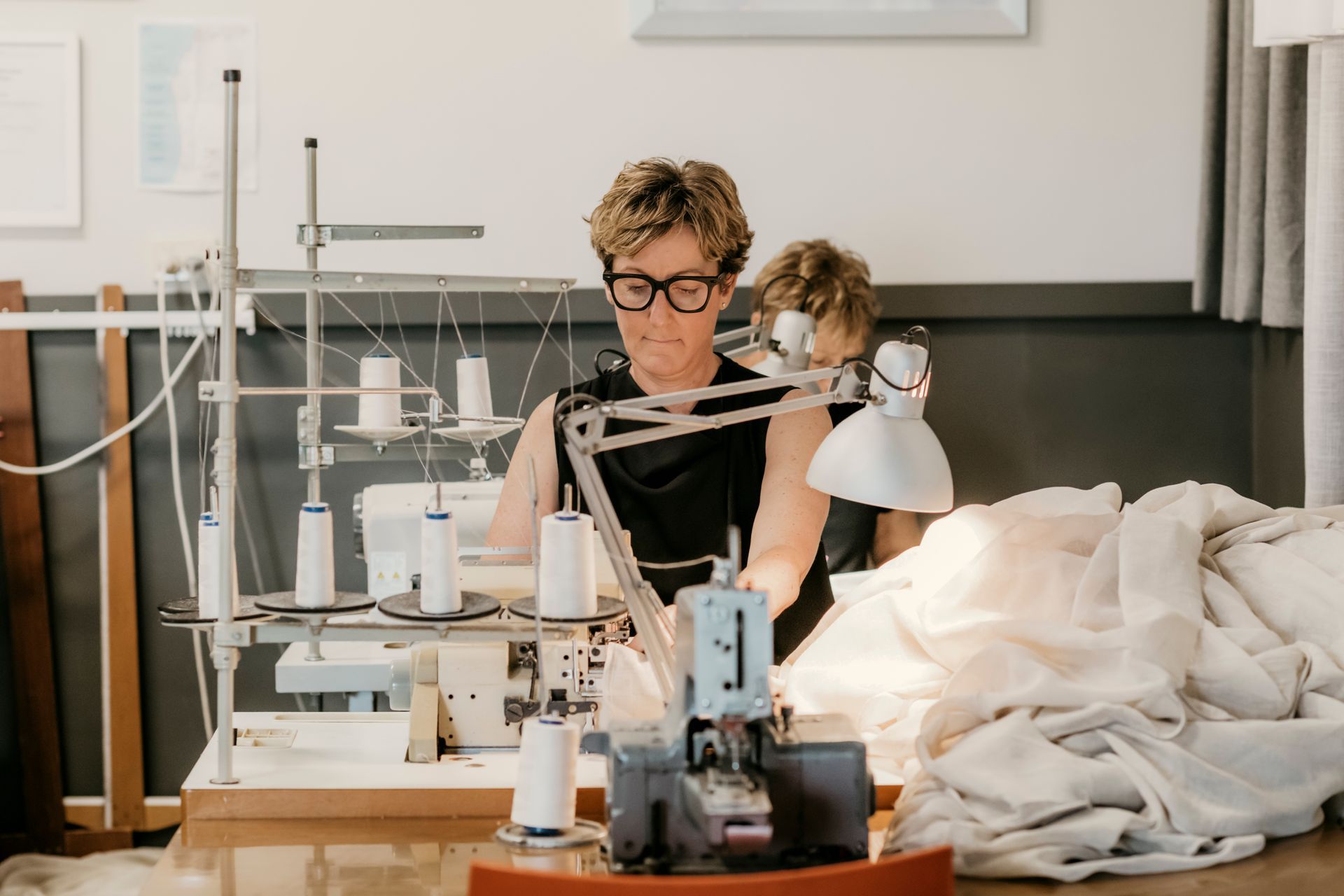 Person sewing at a machine in a bright workshop, with fabric and tools spread across the table. — Curtain Concepts in Dunbible, NSW