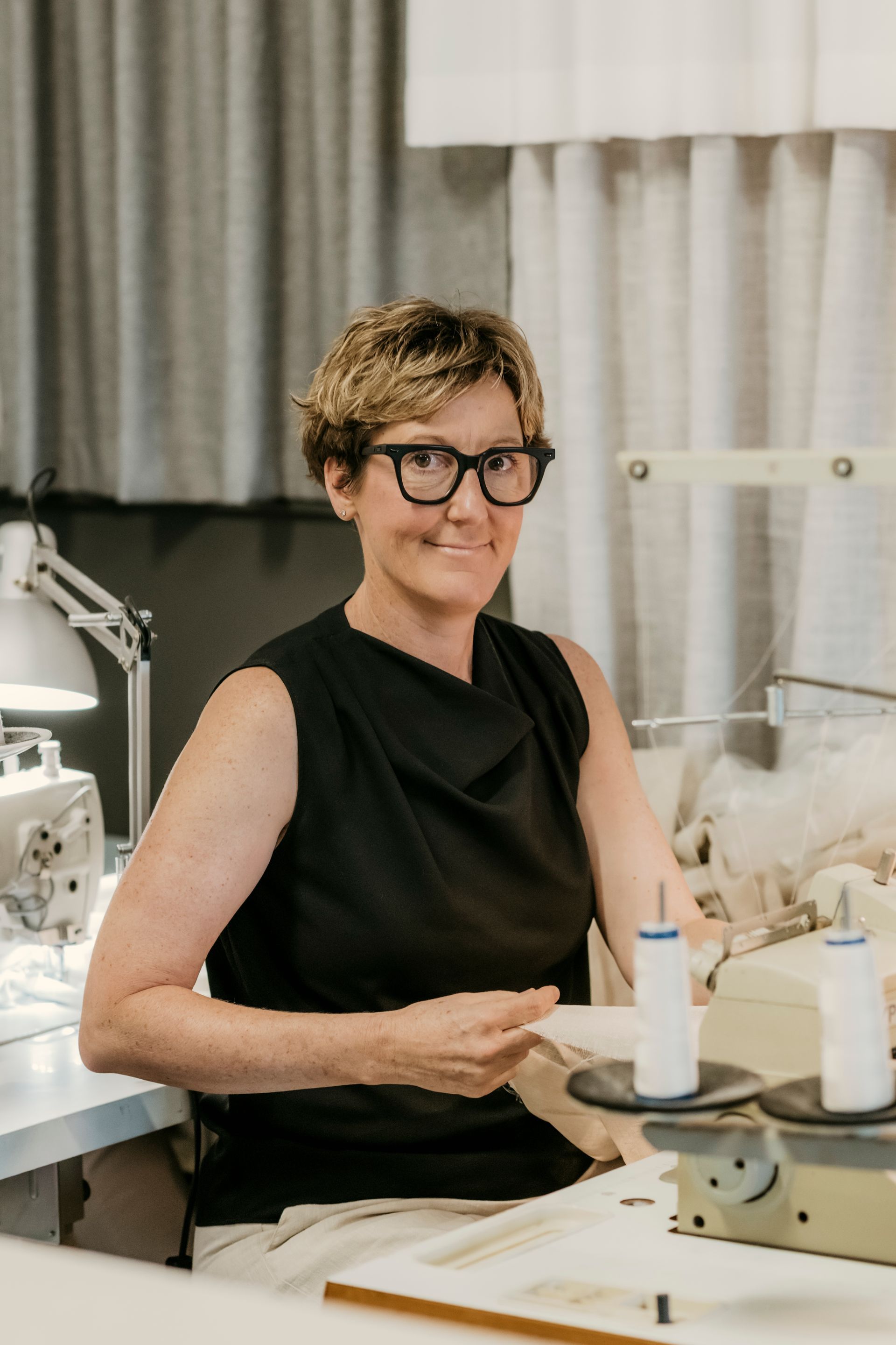 Person smiling at a worktable with sewing equipment in a studio — Curtain Concepts in Dunbible, NSW
