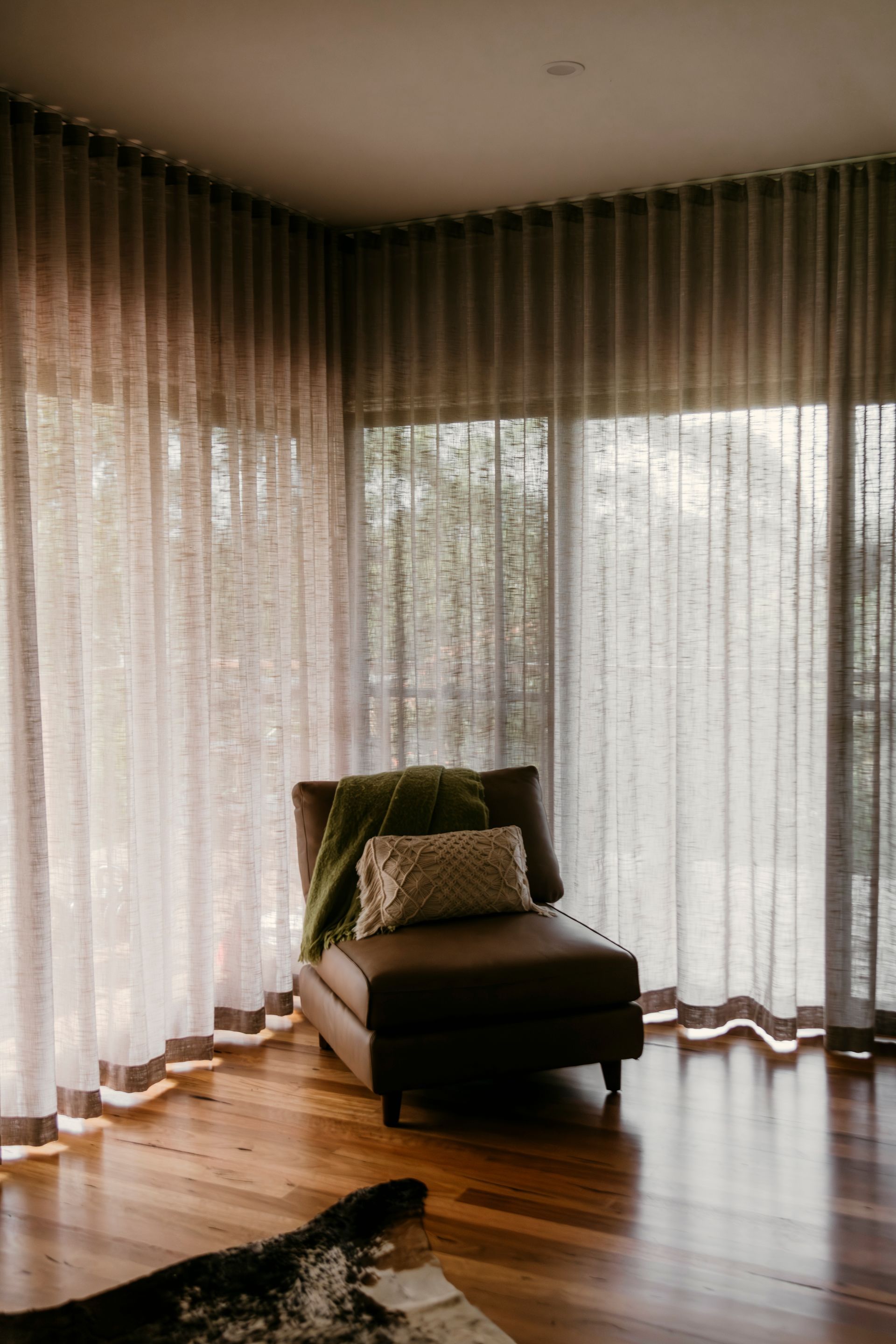 Cozy living room with sheer curtains, sunlight, a cushioned chair, and a hardwood floor — Curtain Concepts in Dunbible, NSW
