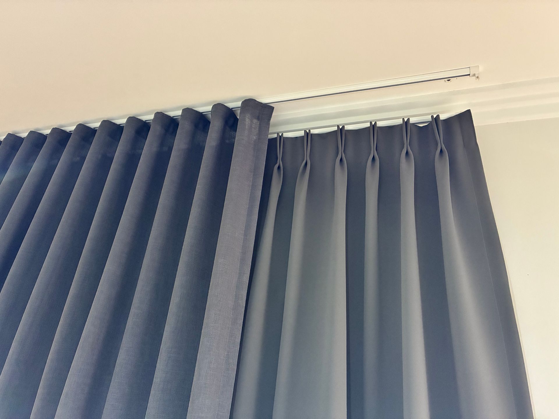 Blue curtains hanging beside a window with white blinds and a curtain rod
