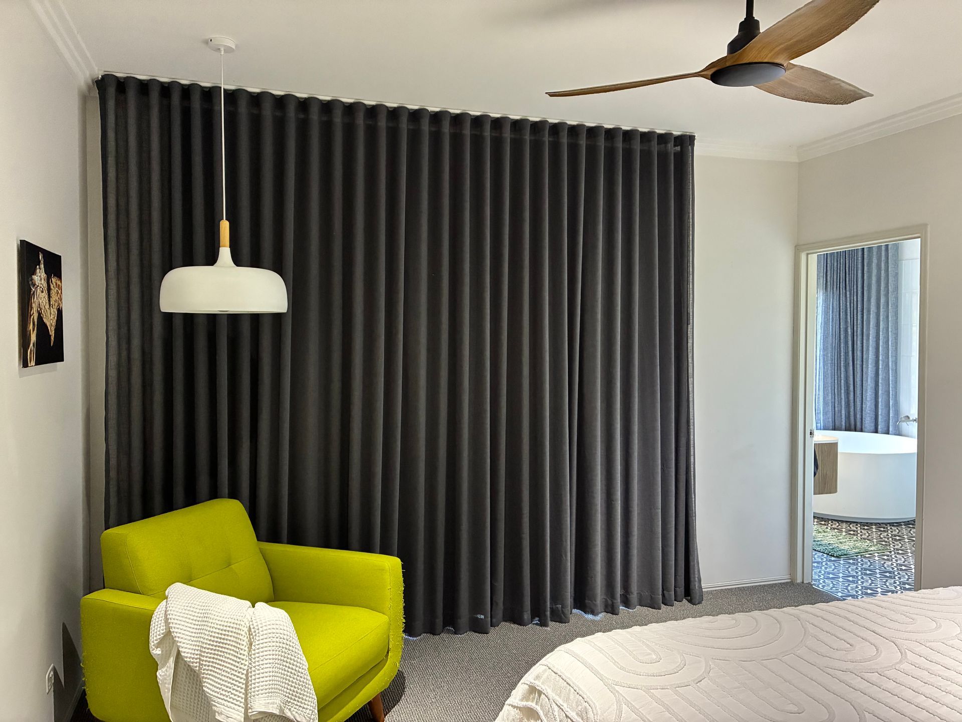 Modern bedroom with dark gray curtains, lime-green chair, white rug, and ceiling fan