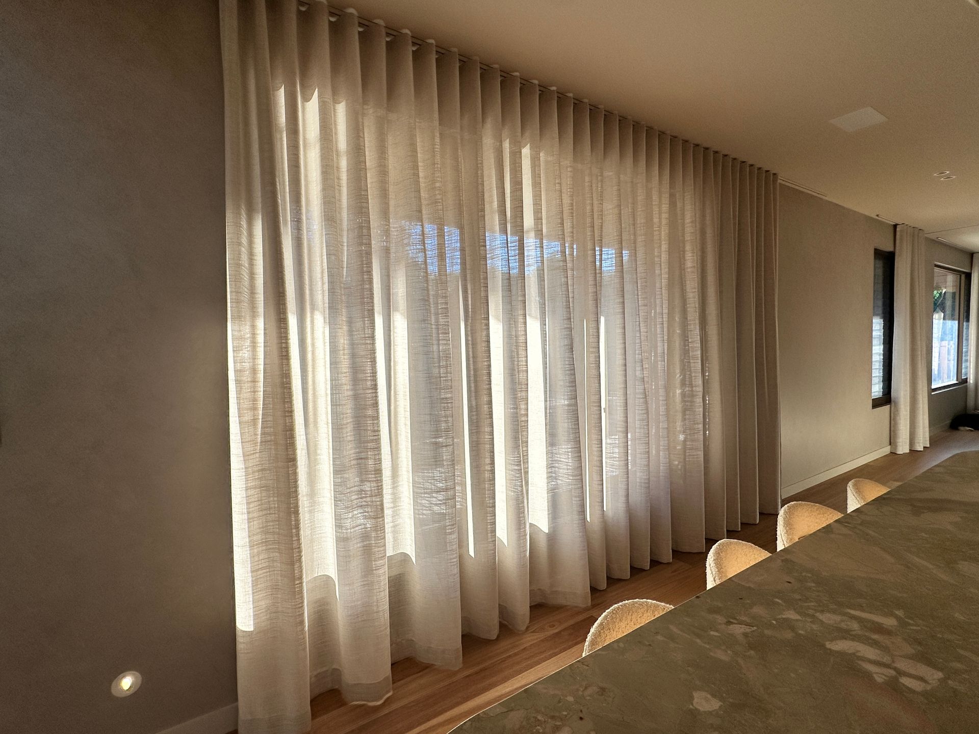 Sunlit hallway with sheer curtains along large windows and a patterned carpet runner