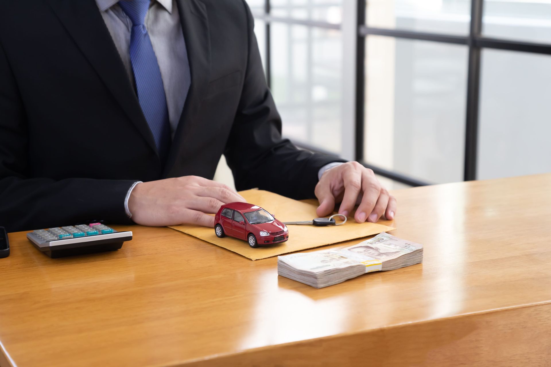 Businessman at a desk with a toy car, calculator, and stack of cash in an office