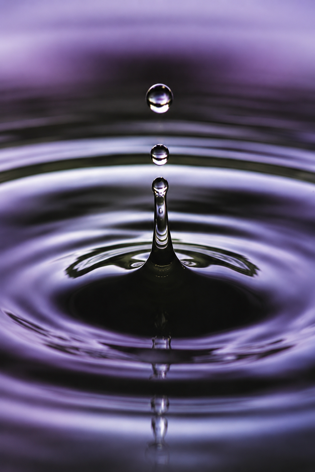 Purple water droplet splashing into rippling water, creating a crown-shaped splash