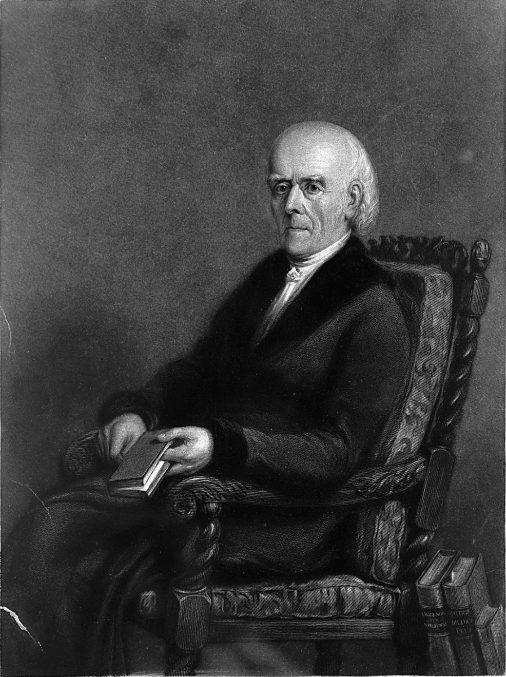 Black-and-white portrait of an elderly man seated in an ornate chair holding a book