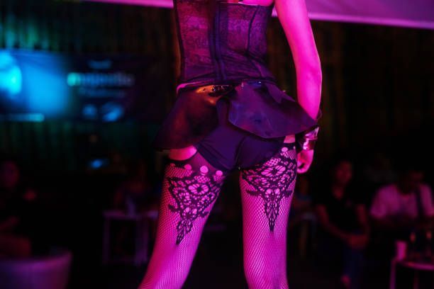 A performer in black lace lingerie and stockings under pink and purple club lights on stage