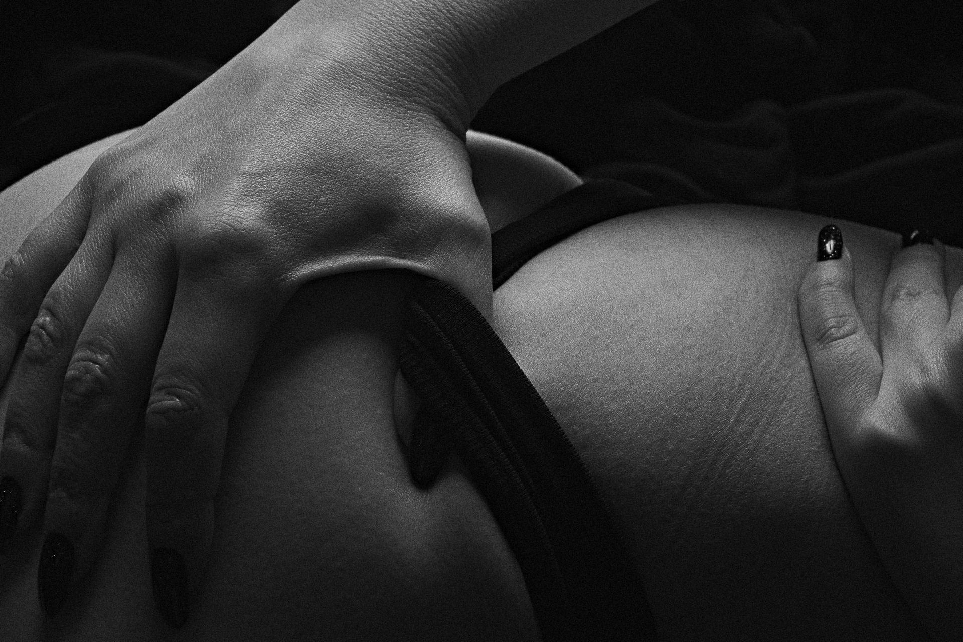 Hands resting on a bare torso in dramatic black-and-white lighting