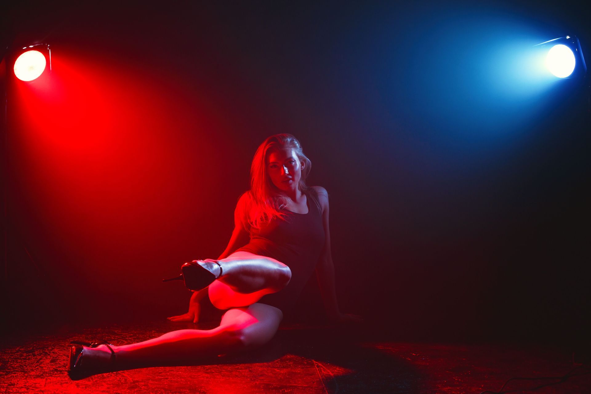Person seated on a dark floor in red and blue spotlight, holding a white object