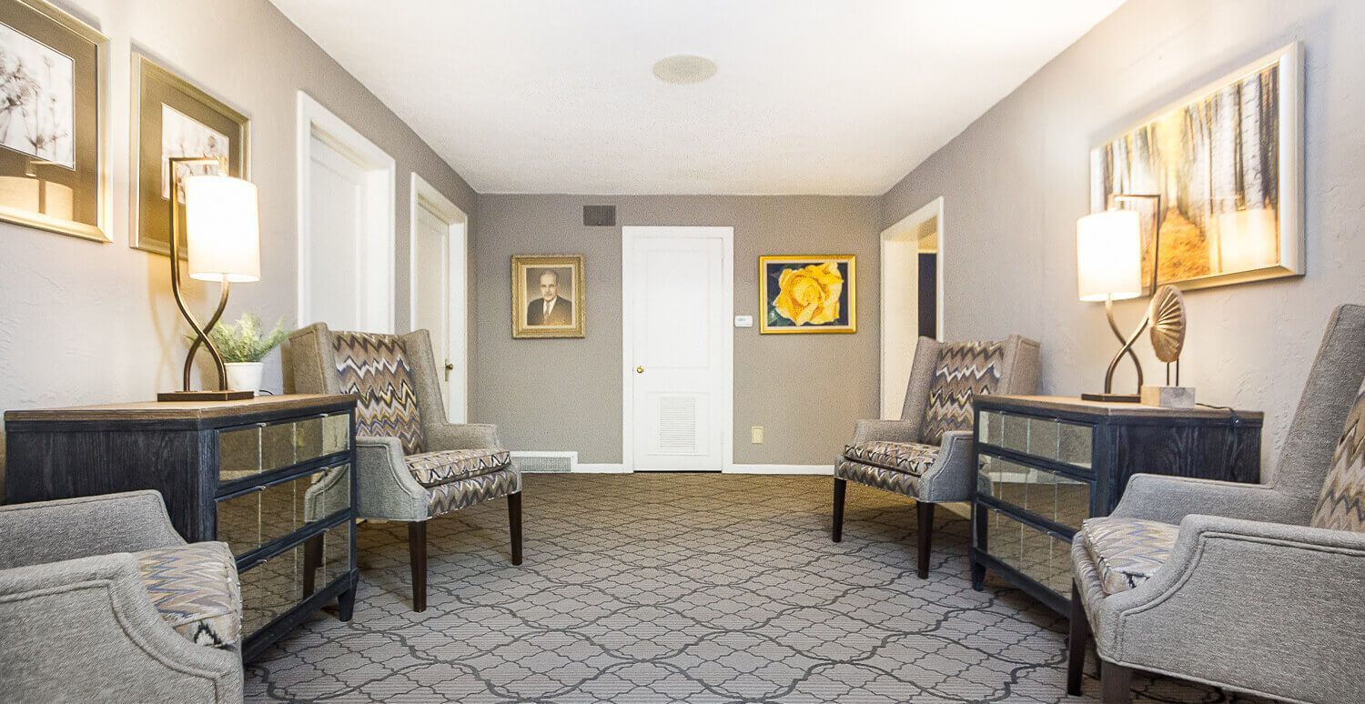 A hallway with chairs , tables , lamps and a painting on the wall.