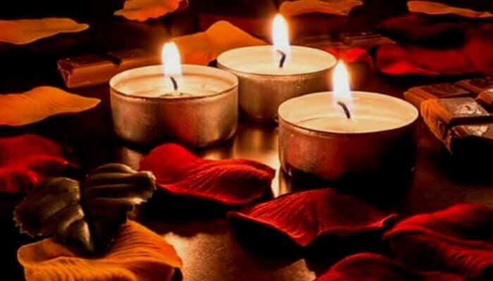 Tres velas encendidas están rodeadas de pétalos de rosa sobre una mesa.