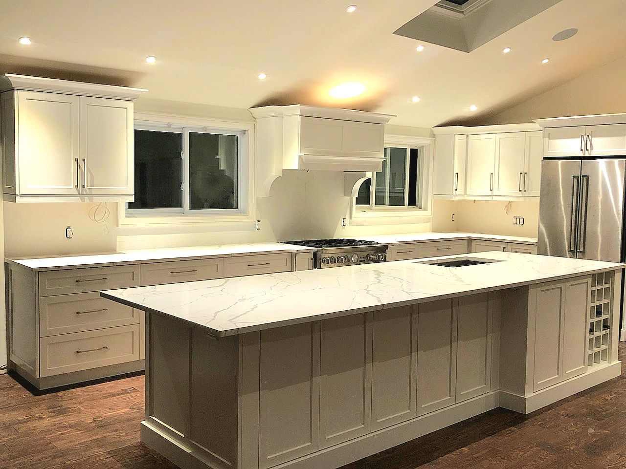 Bright white modern kitchen with large island, stainless steel appliances, and recessed lighting