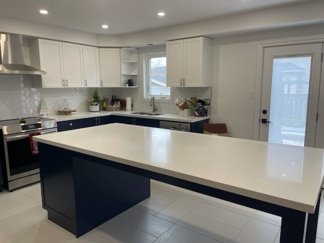 Modern white kitchen with a large island and black base cabinets, stainless steel appliances, and a glass door
