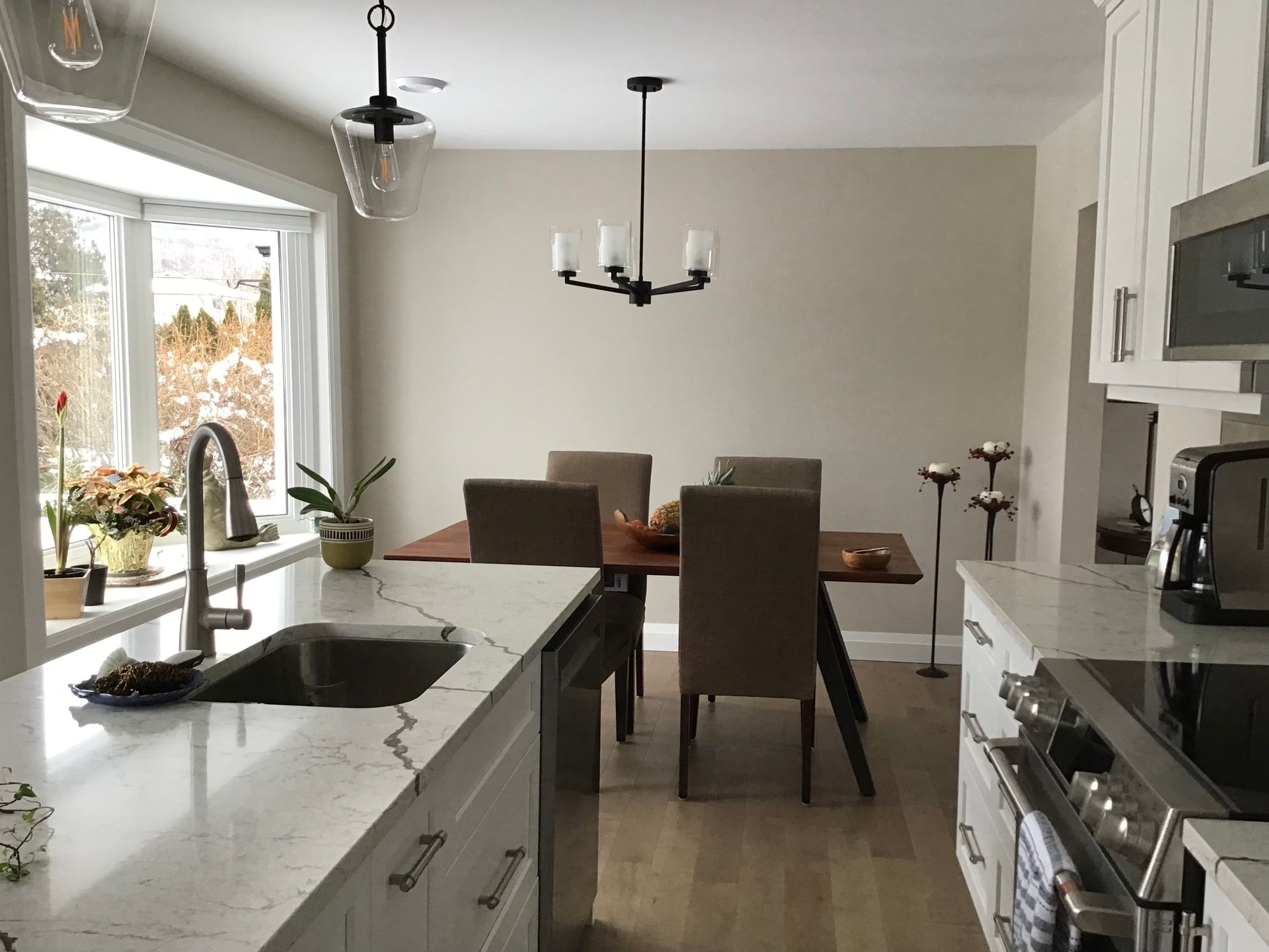 Bright modern kitchen with island, stainless appliances, dining table, and large window view of autumn trees