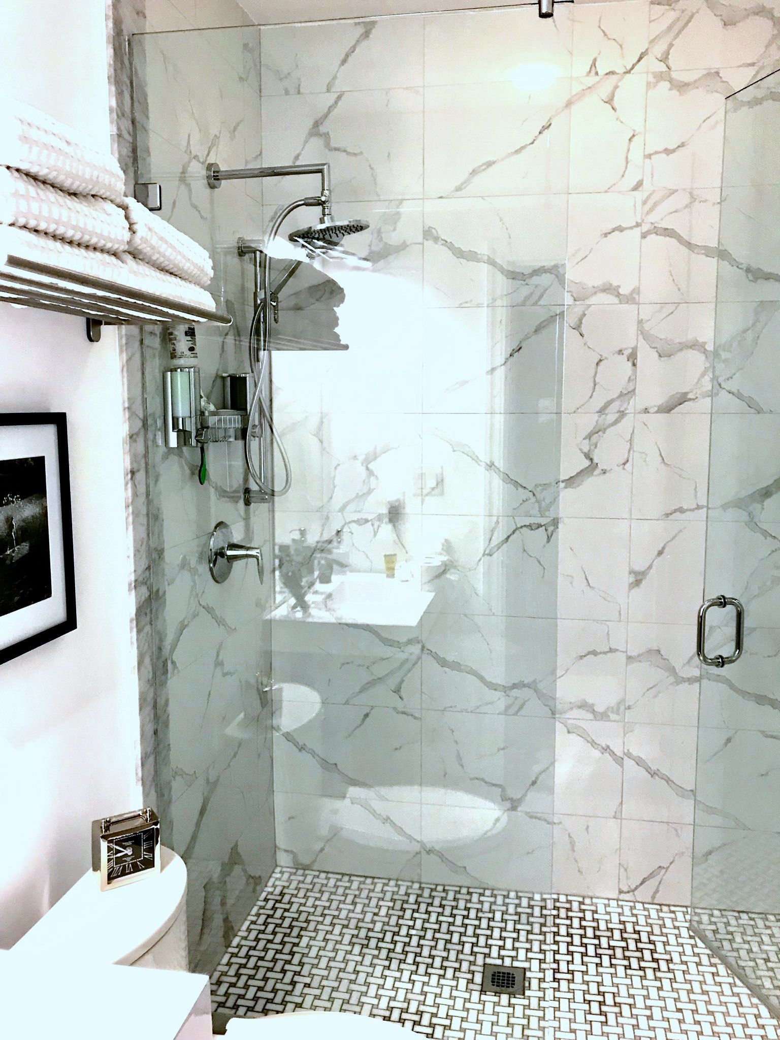 Small white bathroom with a glass shower, marble walls, mosaic floor, and a toilet on the left.
